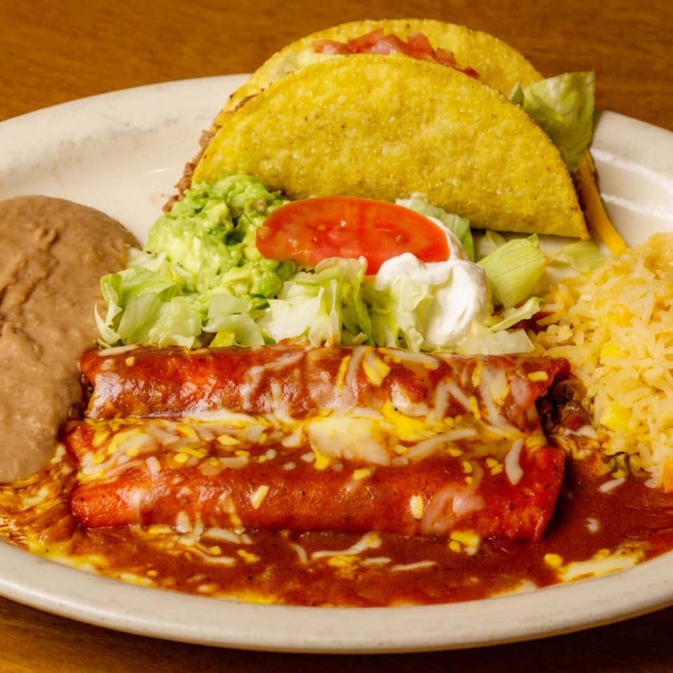 Mexican combination plate with enchiladas, hard-shell tacos, refried beans, guacamole, salad, sour cream, and rice.