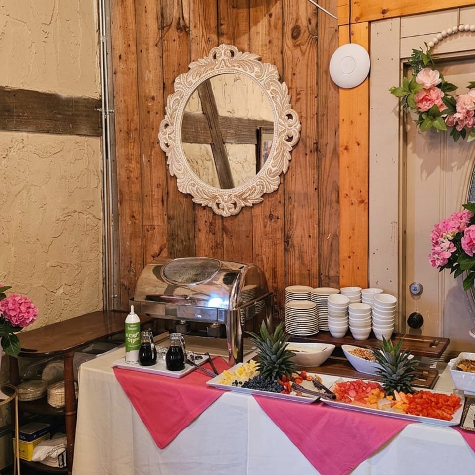Buffet table with fruit, pastries, stacked dishes, and pink hydrangea arrangements in a rustic restaurant dining area.