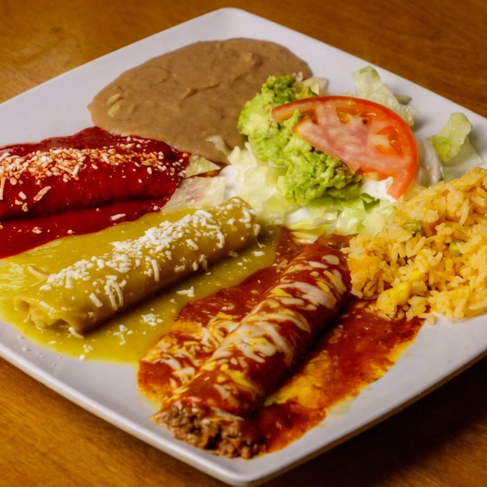 Mexican platter with red, green, and mole enchiladas, refried beans, rice, guacamole, lettuce, and tomato on a white plate.