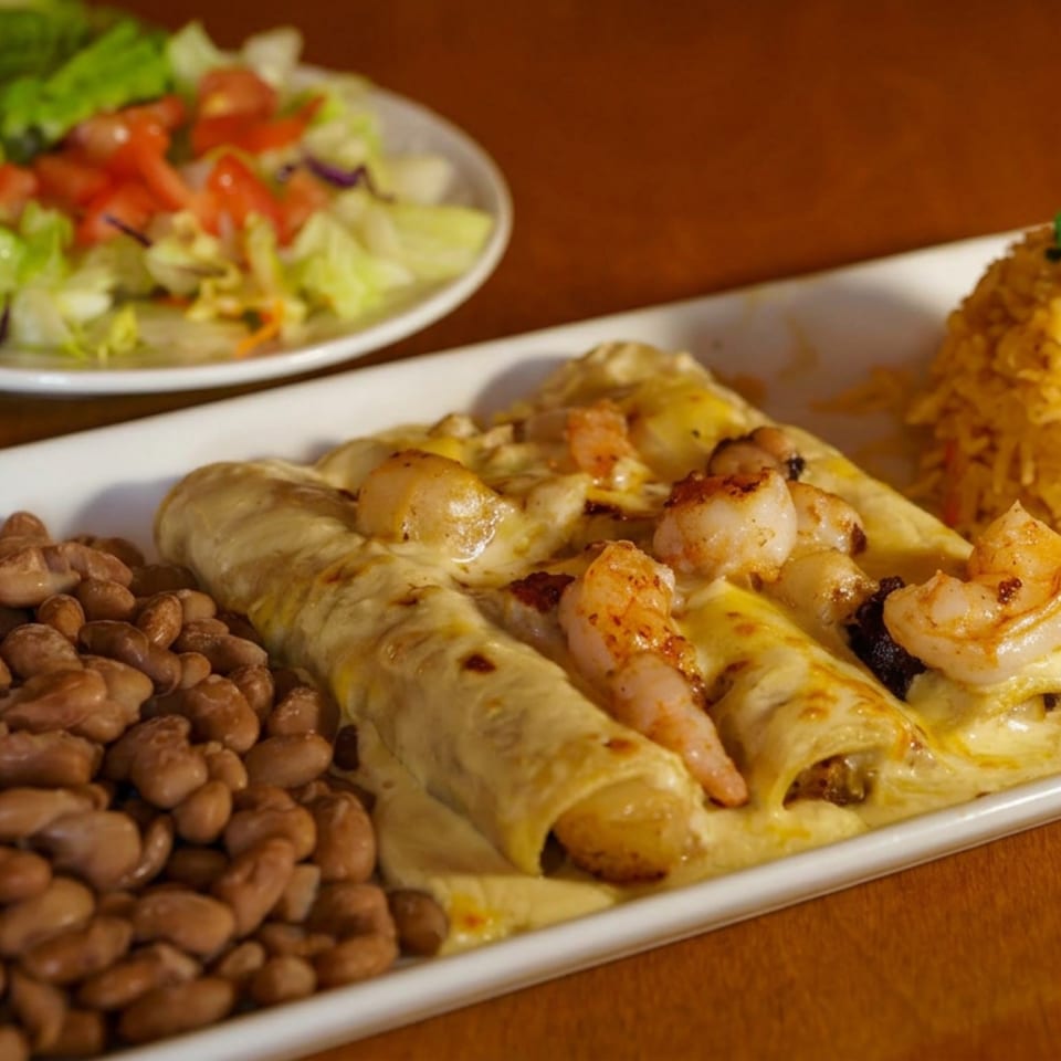 Mexican platter featuring shrimp enchiladas with melted cheese, pinto beans, yellow rice, and a side salad.