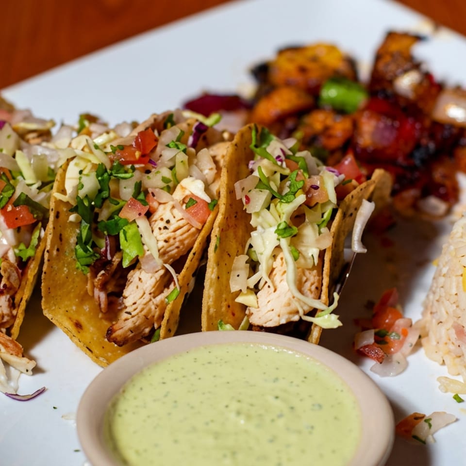Three chicken tacos with cabbage, pico de gallo, grilled vegetables, black beans and rice, served with creamy green sauce.