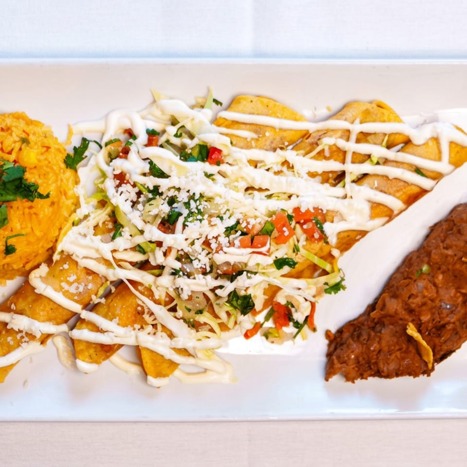 Mexican-inspired platter with yellow rice, sauced enchiladas topped with vegetables and cheese, and a crispy fried taco.